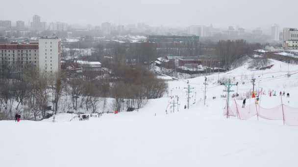 Σκιέρ κατεβαίνουν το λόφο κοντά στην πόλη το χειμώνα συννεφιασμένη μέρα — Αρχείο Βίντεο