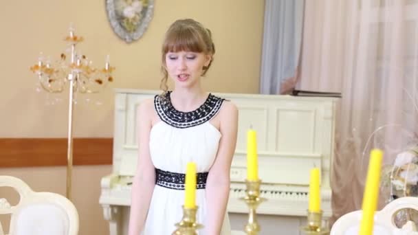 Chica bonita en vestido blanco recita cerca de la mesa con velas amarillas — Vídeos de Stock