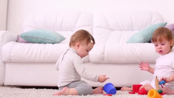 Twee mooie meisjes zitten op zachte tapijt en spelen met speelgoed in de buurt van Bank — Stockvideo