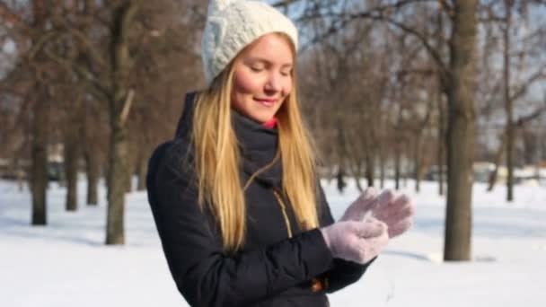 Young woman in hat holds in hands snow in park at winter day — Stock Video