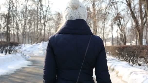 Junge Frau mit weißem Hut spaziert am Wintertag im Park — Stockvideo