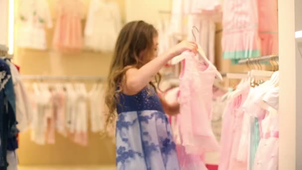 Девушка смотрит на одежду и берет юбку с блузкой в галерее — стоковое видео