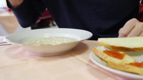 Manos de hombre comiendo gachas en cantina con sillas rojas — Vídeos de Stock