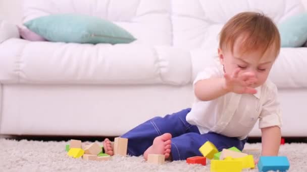 Bebê bonito senta-se no tapete macio e quebra torre de brinquedos tinker — Vídeo de Stock