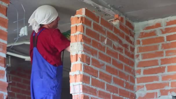 Hombre trabajador en ropa de trabajo rompe la pared de ladrillo rojo en el apartamento — Vídeo de stock