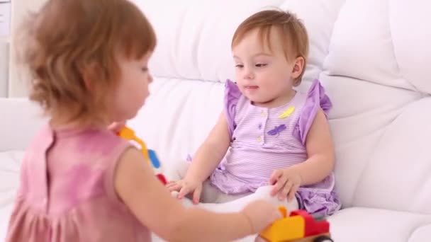 zwei kleine Mädchen in Kleidern spielen mit Spielzeugautos auf weißem Sofa