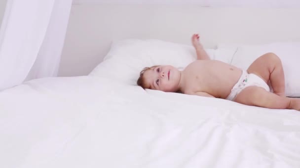 Gelukkig weinig baby in luier op witte bed ligt en draait — Stockvideo