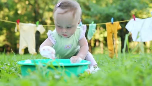 Baby touches and eats foam in basin on grass — Stock Video