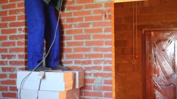 Работник в рабочей одежде делает отверстие в стене с большим перфоратором — стоковое видео