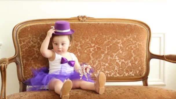 Baby flicka i balett kjol sitta på vintage soffa med hatt — Stockvideo