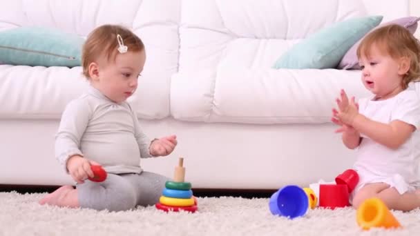 Zwei hübsche Mädchen sitzen auf Teppich und spielen mit Spielzeug in der Nähe von Sofa — Stockvideo