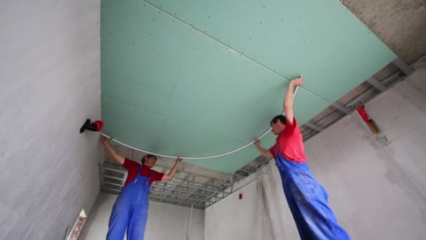 Рабочие устанавливают потолок в новой квартире без отделки — стоковое видео