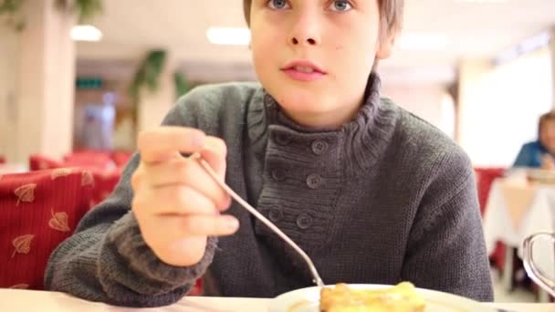 Schöner Junge isst Auflauf in Kantine mit roten Stühlen — Stockvideo