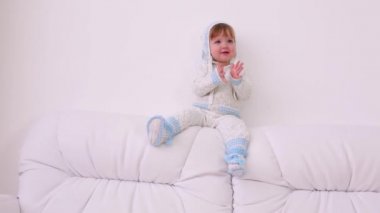 Şapka ve örme takım elbise sevimli bebek evde kanepeve alkışlar oturur