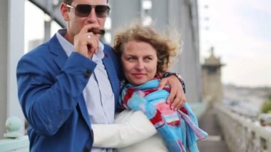 Woman hugs man smoking cigar and strokes his cheek on bridge