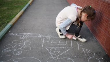 Küçük sevimli kız sokakta tebeşir ile asfalt üzerinde resim çizer