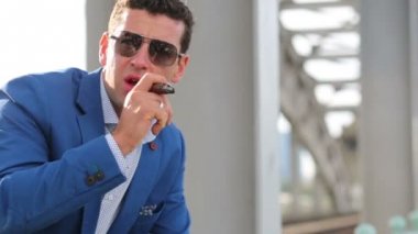 mavi ceket ve güneş gözlüğü adam demiryolu köprüsünde puro içiyor