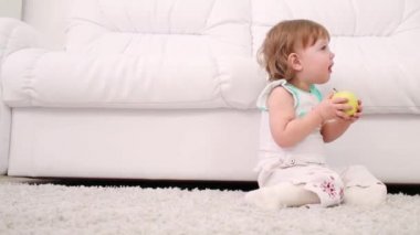Sevimli küçük kız halı üzerinde oturur ve evde elma yiyor
