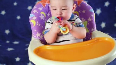 Bebek çocuk mama sandalyesine oturur ve diş çıkarma halkası nibbles.