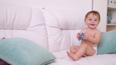 Yastıklı beyaz kanepede oyuncak gülümsüyor bebek bezi küçük çocuk