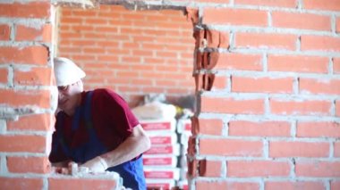 Worker in workwear makes doorway in red brick wall by perforator