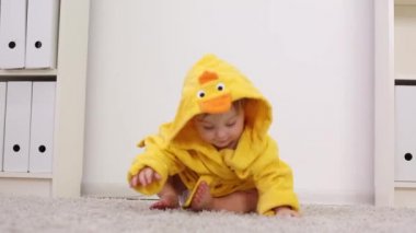 Sarı bornoz standları küçük sevimli bebek duruyor ve beyaz halı üzerinde bırakır