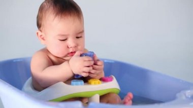 Küçük oğlan mavi bir küvette elinde bir oyuncakla oturuyor