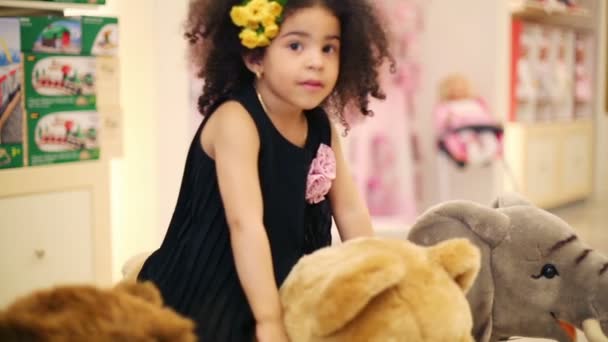 Маленька мила дівчинка гойдається на м'якому іграшковому ведмедику в магазині з іграшками — стокове відео