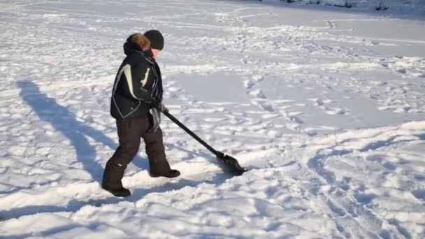 Jongen in zwart verwijdert sneeuw door shovel voor het maken van pad op de winter — Stockvideo