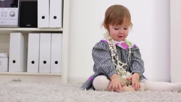 Little girl in dress puts on and removes beads on carpet at home — Stock Video