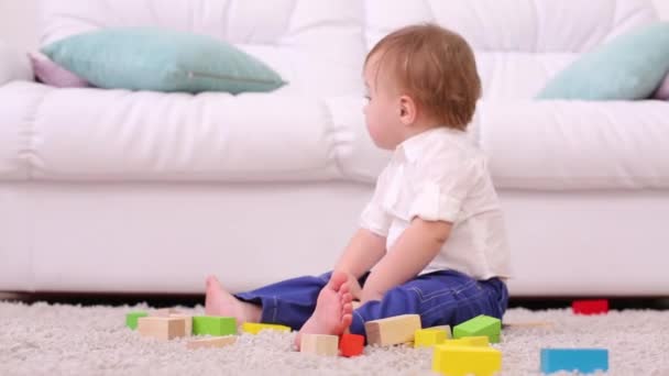 Bebê bonito senta-se no tapete macio entre brinquedos tinker e gritos — Vídeo de Stock