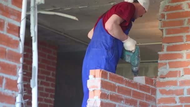 Jovem trabalhador em vestuário de trabalho quebra parede de tijolo vermelho em novo apartamento — Vídeo de Stock