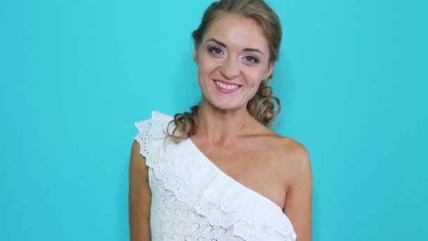Chica joven feliz en una blusa blanca se para junto a una pared azul — Vídeo de stock