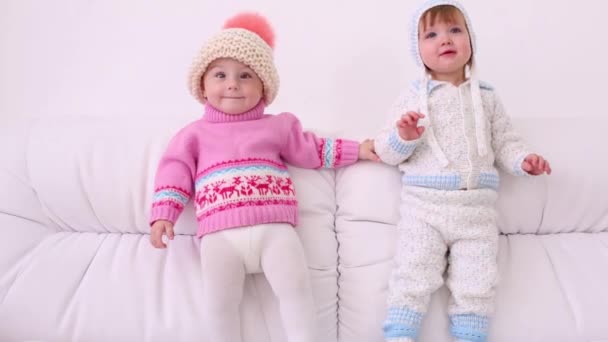 Deux petits enfants en chapeaux et vestes tricotées se tient sur canapé blanc — Video