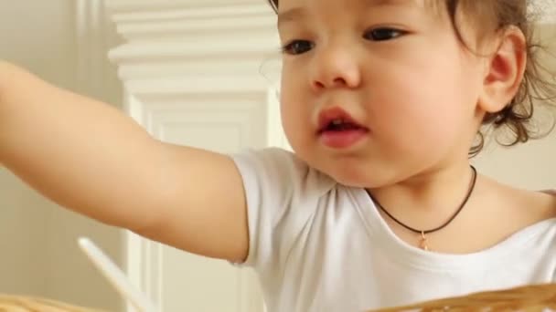 Χαριτωμένο μωρό αγόρι βγάζει κουτάλι της καλάθι σε λευκό δωμάτιο — Αρχείο Βίντεο