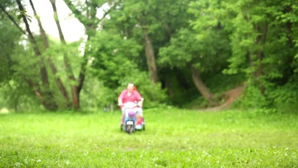 Homem em scooter com reboque entra e cruza gramado verde gramado . — Vídeo de Stock