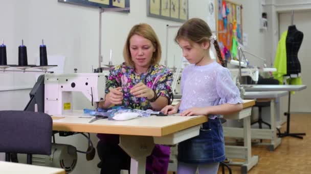 Alfaiate fêmea senta-se à mesa com máquina de costura e ensina menina — Vídeo de Stock