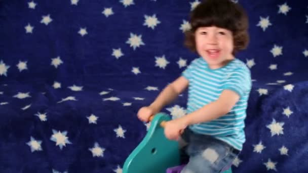 Little boy joyfully rides rocking horse in room next to sofa. — Stock Video