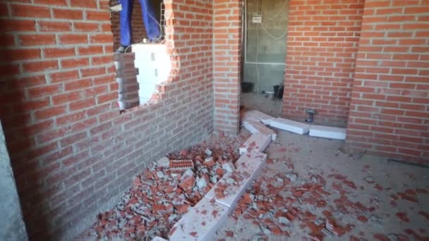Hombre trabajador en ropa de trabajo rompe la pared de ladrillo rojo en nuevo apartamento — Vídeos de Stock