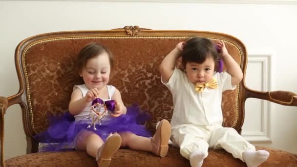 Baby boy and girl sit on couch with toy crown and hat — Stock Video