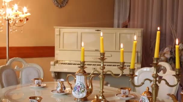 Table with set of porcelain dishes and lighted candles and lamp — Stock Video