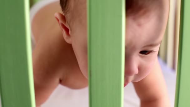 Närbild ansikte baby pojke som kryper i trä lekhage. — Stockvideo