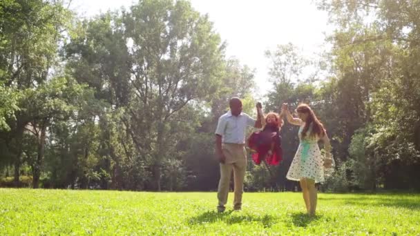 Los padres levantan a su hija de la mano en el parque de verano — Vídeos de Stock