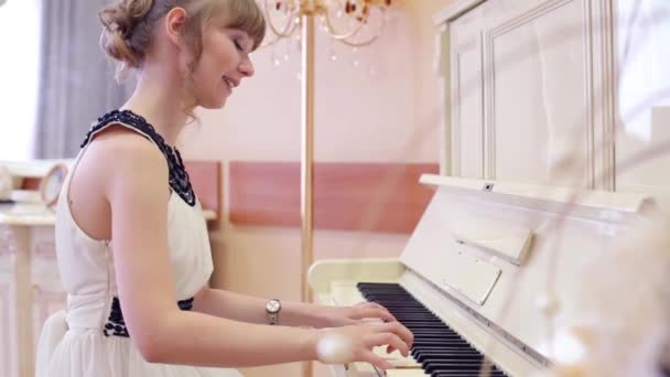 Lächelndes Mädchen im weißen Kleid spielt weißes Klavier im hellen Raum — Stockvideo