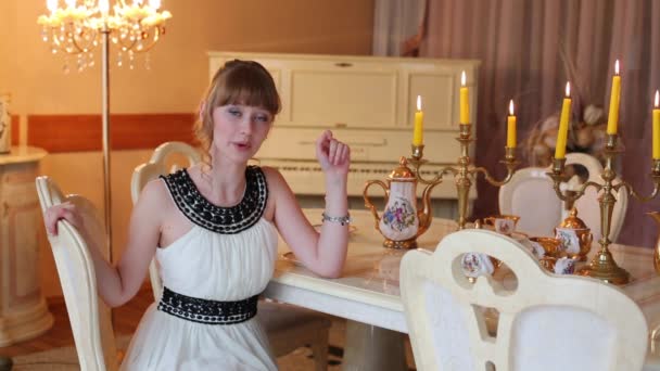 Hermosa chica en vestido se sienta a la mesa con porcelana y habla — Vídeos de Stock