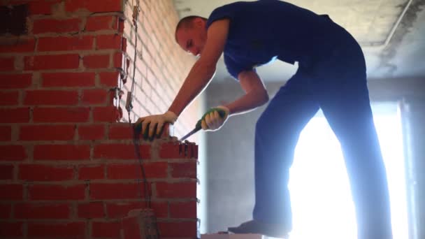 Trabalhador em vestuário de trabalho quebra parede de tijolo vermelho no novo apartamento — Vídeo de Stock