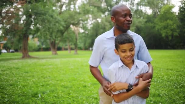 Отец обнимает и щекочет сына в парке в летний день — стоковое видео
