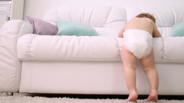 Повернення дитини в підгузник, що спускається з білого дивана вдома — стокове відео