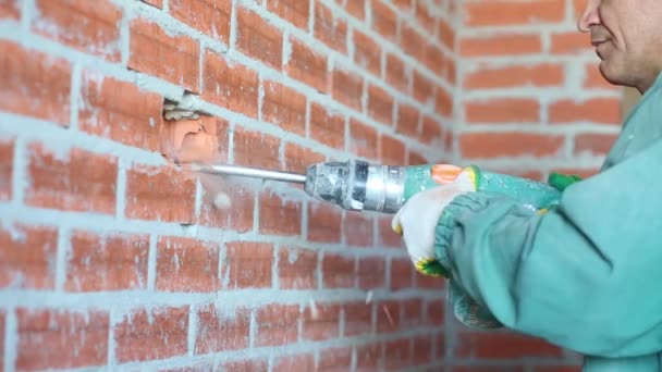 Mains sur l'homme en vert tenant perforateur brisant mur de briques rouges — Video