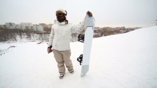 Snowboarder girl in glasses standing on a slope and points toward — Stock Video